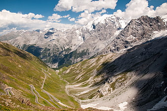 Winding mountain road through alpine valley with snow-capped peaks