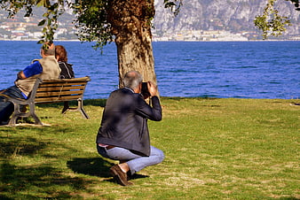 Senior man photographing couple on bench by lake