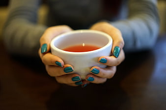 Hands holding white teacup with hot tea and teal nail polish