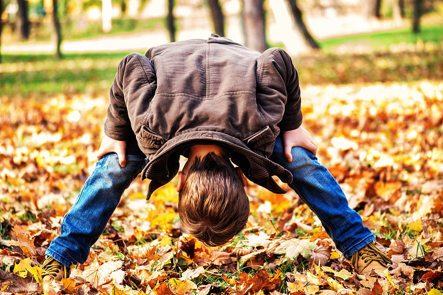 Toddler looking through legs in autumn leaves