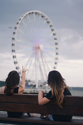 Two women pointing at a blurred Ferris wheel from a bench