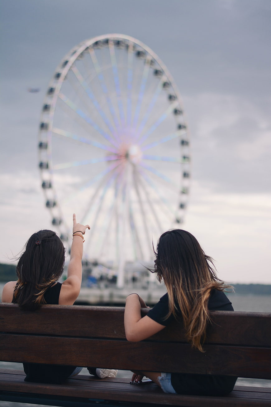 Two women pointing at a blurred Ferris wheel from a bench
