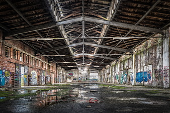 Abandoned industrial warehouse interior with graffiti and puddles