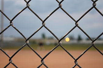 Chain link fence with blurred baseball field and sunset background