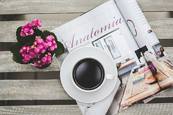 Top view of coffee cup, magazine, and pink flowers on wooden table