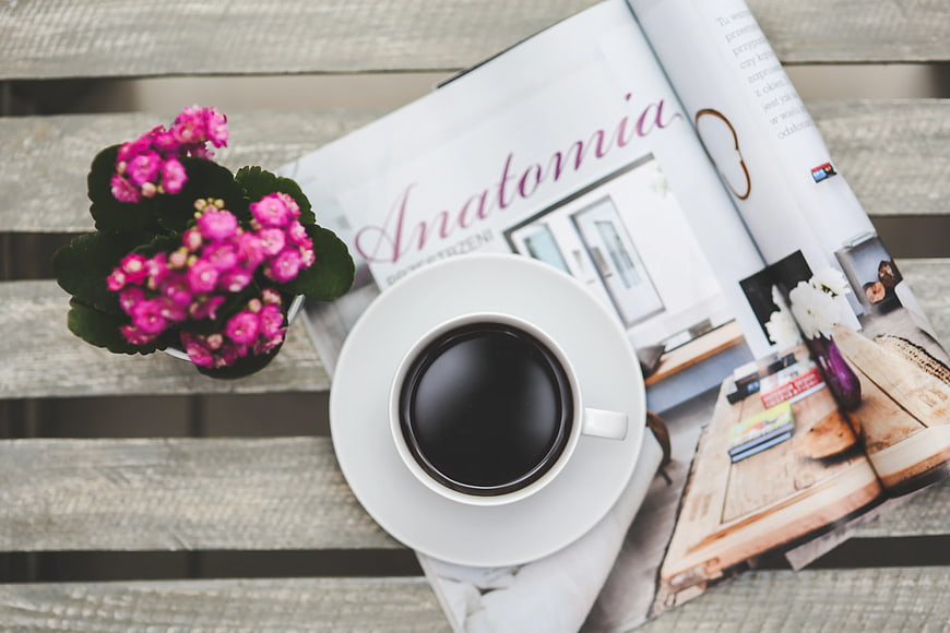 Top view of coffee cup, magazine, and pink flowers on wooden table