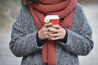 Woman holding coffee cup with flower in autumn scarf
