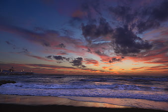 Dramatic purple and orange sunset over ocean waves and beach