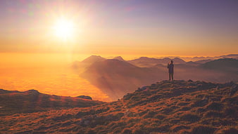 Silhouette of person standing on mountain peak at sunrise