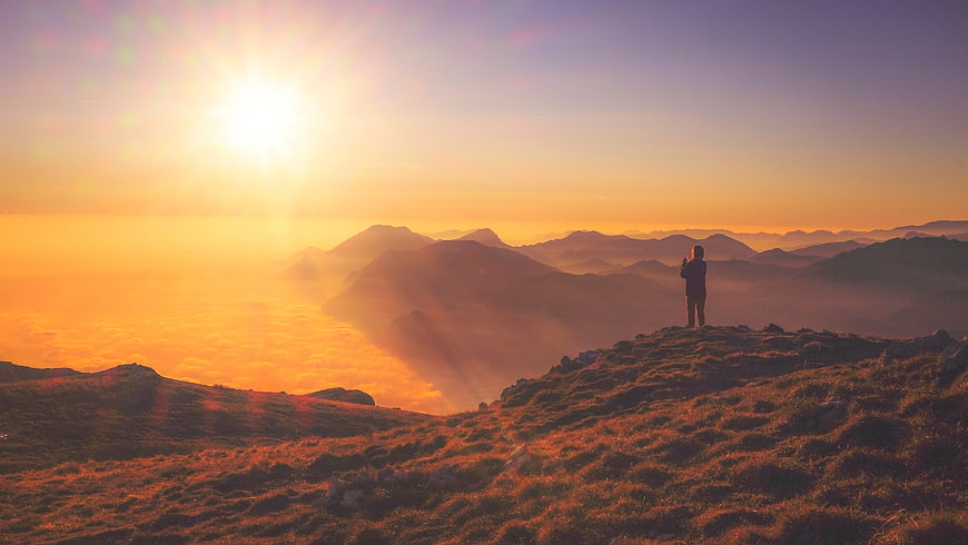 Silhouette of person standing on mountain peak at sunrise