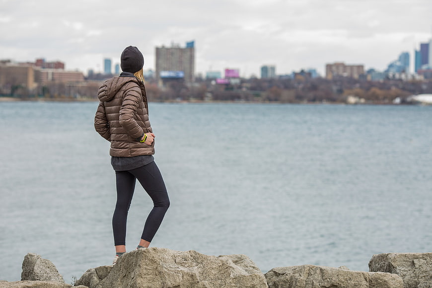 Woman in winter jacket standing on rocks overlooking city skyline