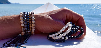 Hand holding artisanal bead bracelets on a surfboard near the ocean
