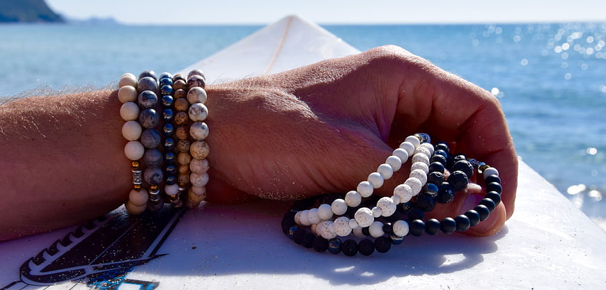 Hand holding artisanal bead bracelets on a surfboard near the ocean