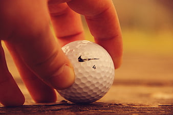 Close-up of hand placing Nike golf ball on wood