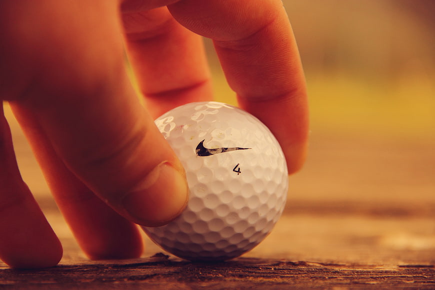 Close-up of hand placing Nike golf ball on wood