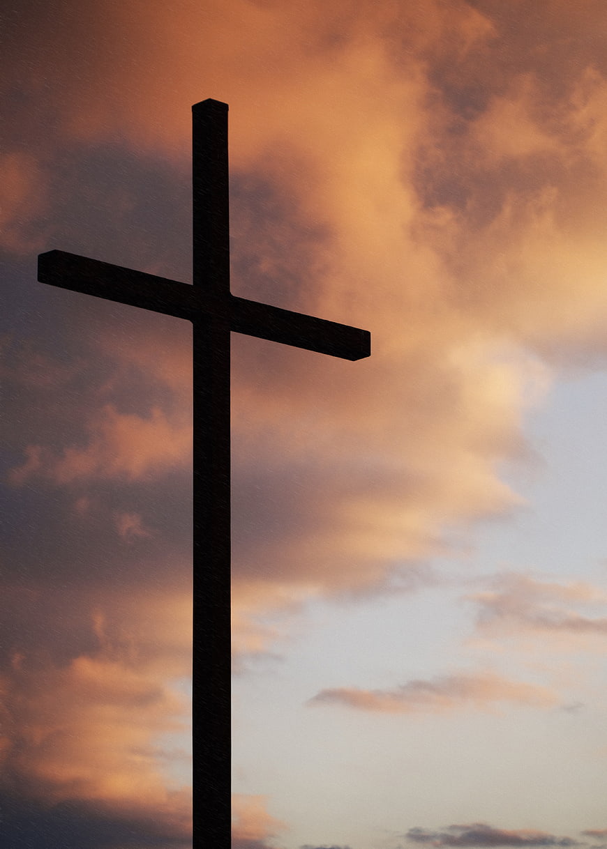 Silhouette of a cross against a dramatic sunset sky