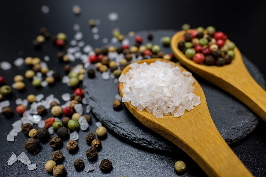 Wooden spoons with coarse salt and mixed peppercorns on dark slate