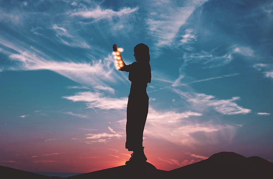 Woman silhouette holding glowing lights against sunset sky