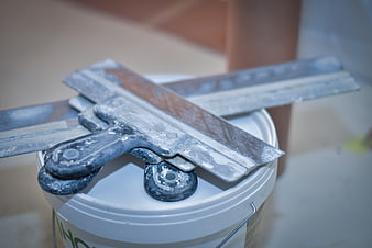 Close-up of metal trowels on a white paint bucket