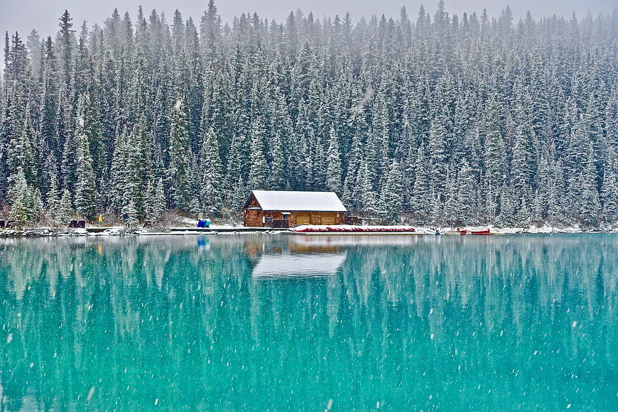 Snowy cabin on turquoise lake with pine forest