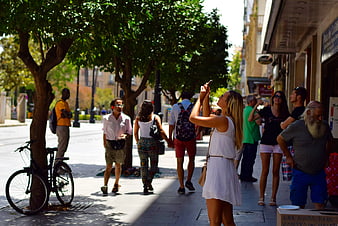 Woman taking photo on sunny city street with pedestrians