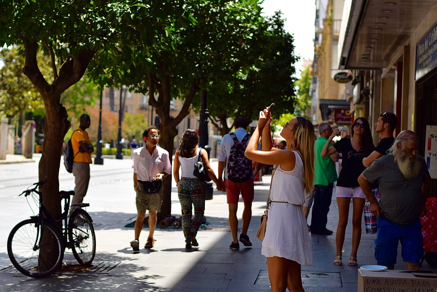 Woman taking photo on sunny city street with pedestrians