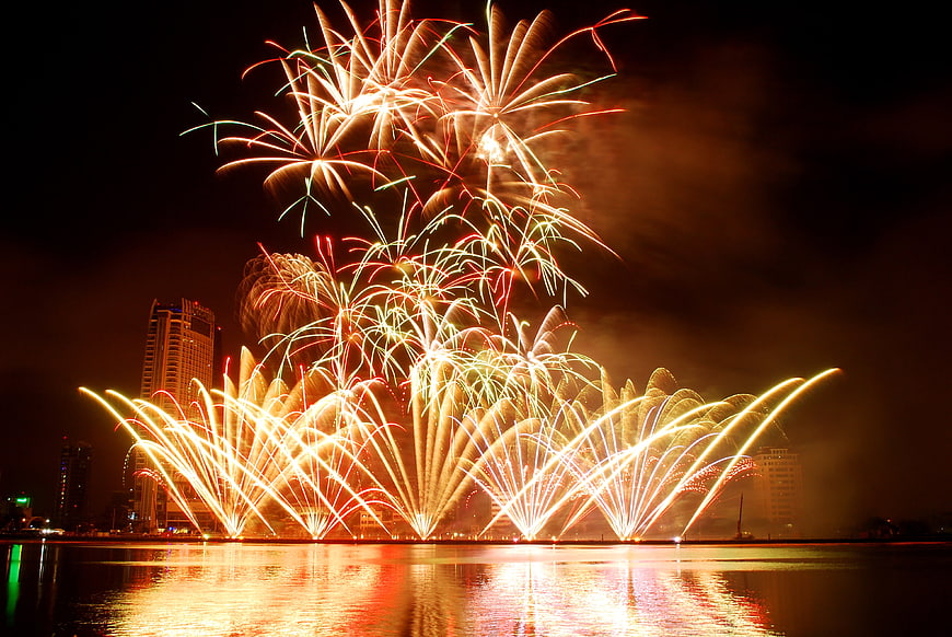 Vibrant Fireworks Display Over Water With City Skyline At Night