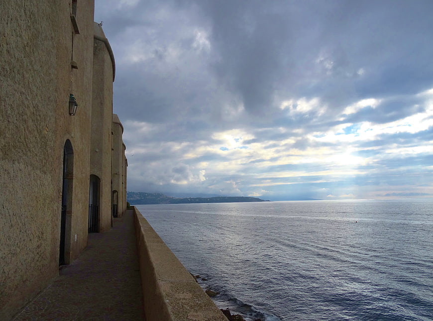Coastal walkway with stone buildings and dramatic cloudy sky