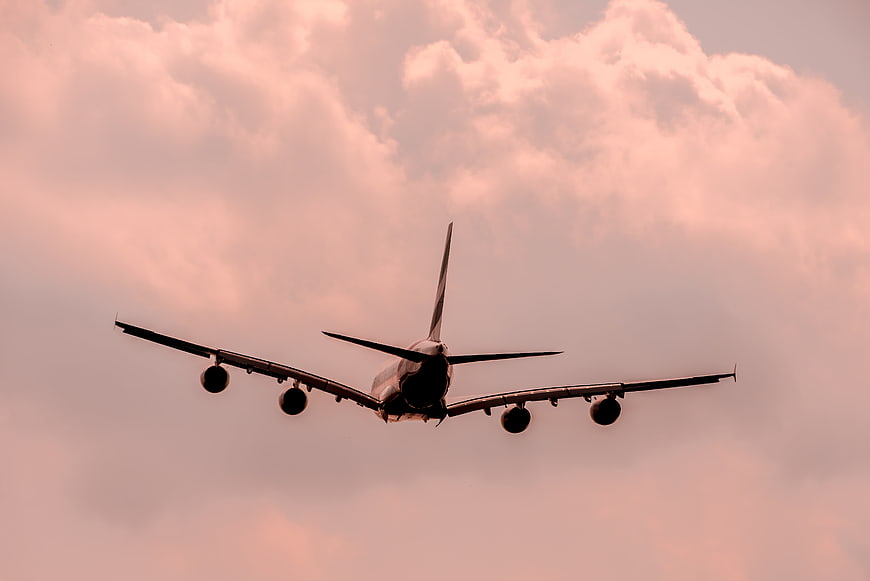 Four-engine airplane landing against pink sunset clouds