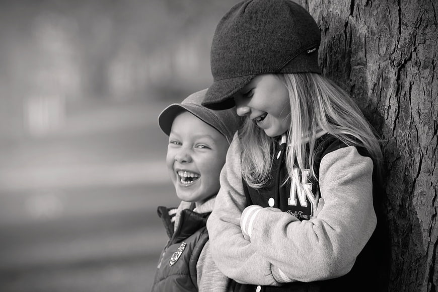 Laughing children leaning against tree in black and white