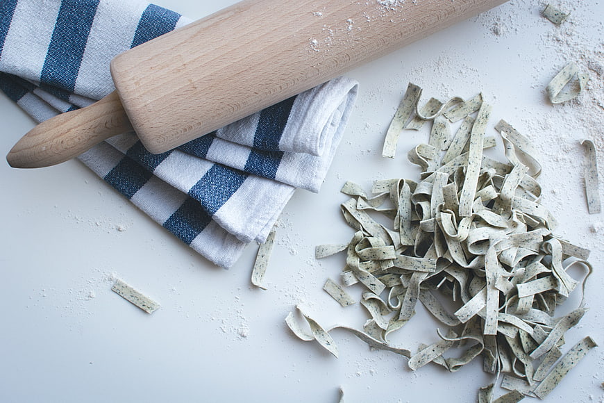 Fresh handmade pasta with rolling pin and flour on white background