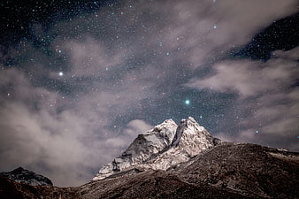 Snowy Mountain Peak Under Starry Night Sky with Clouds