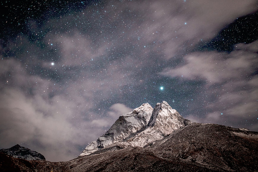 Snowy Mountain Peak Under Starry Night Sky with Clouds