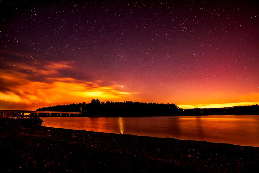 Starry Night Sky Over River with Vibrant Orange Clouds
