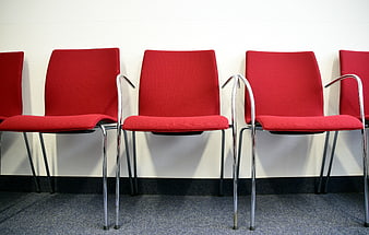 Row of empty red chairs against a white wall in a waiting area