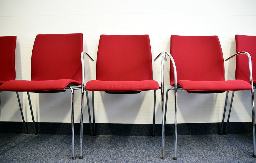 Row of empty red chairs against a white wall in a waiting area