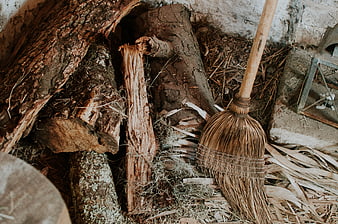 Rustic straw broom leaning against old wooden logs