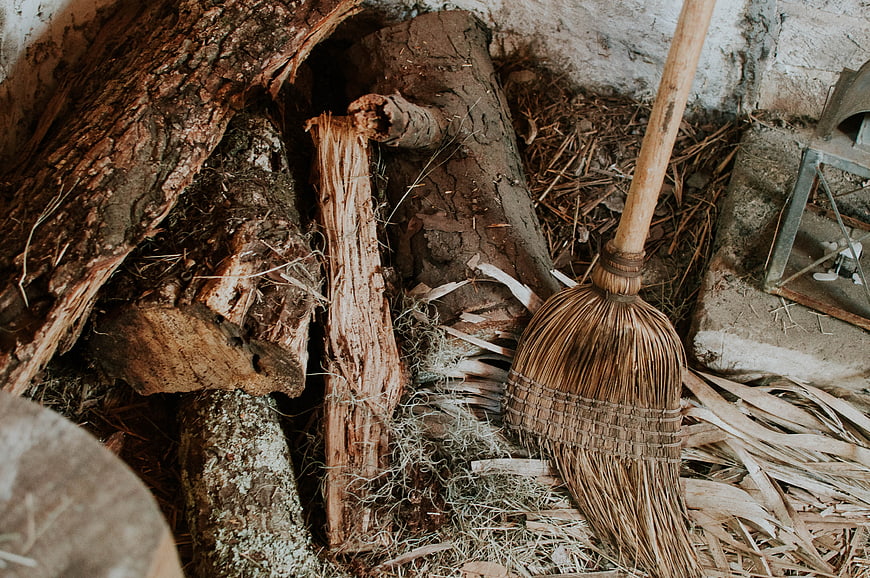 Rustic straw broom leaning against old wooden logs