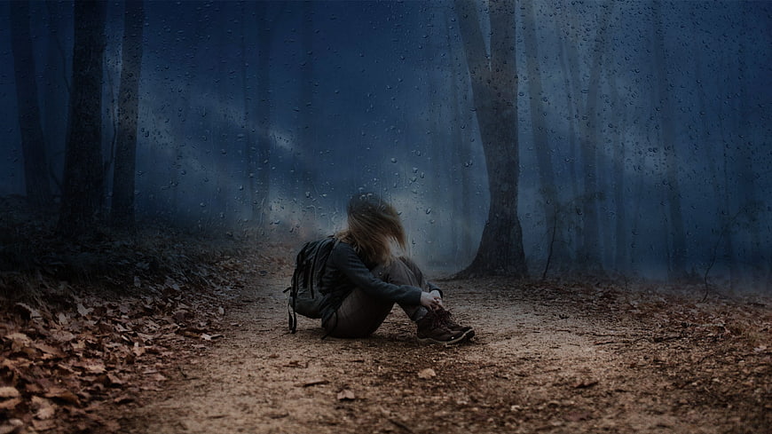Lonely hiker sitting on a rainy forest path in the mist