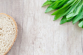 Fresh bread slice and green leaves on wooden background