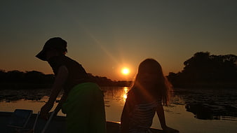 Silhouetted children on a boat at sunset in the Okavango Delta