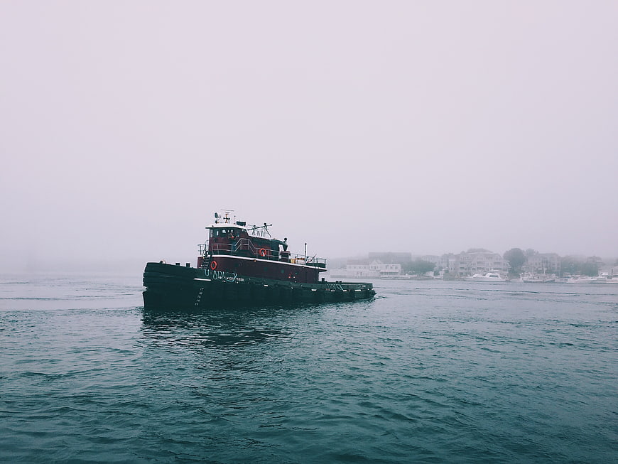 Red Tugboat on Foggy Ocean with Coastal Town