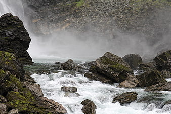 Misty waterfall crashing into rocky river rapids