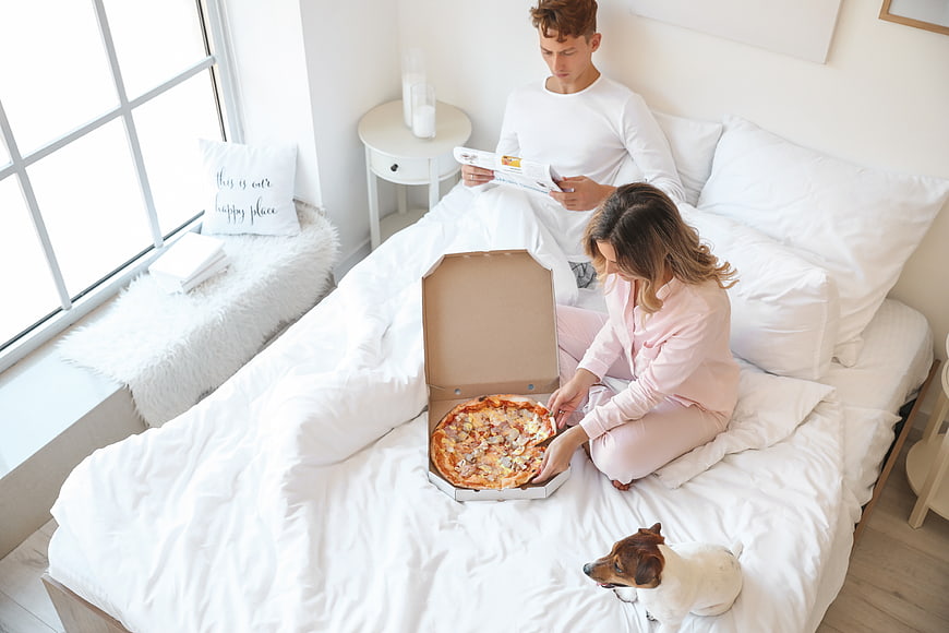 Couple eating pizza in bed with dog
