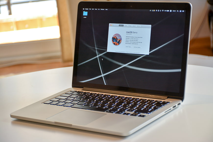 Silver MacBook Pro displaying macOS Sierra system information on a white desk