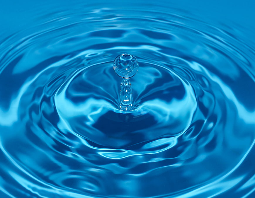 Close-up of a water droplet creating ripples in blue water