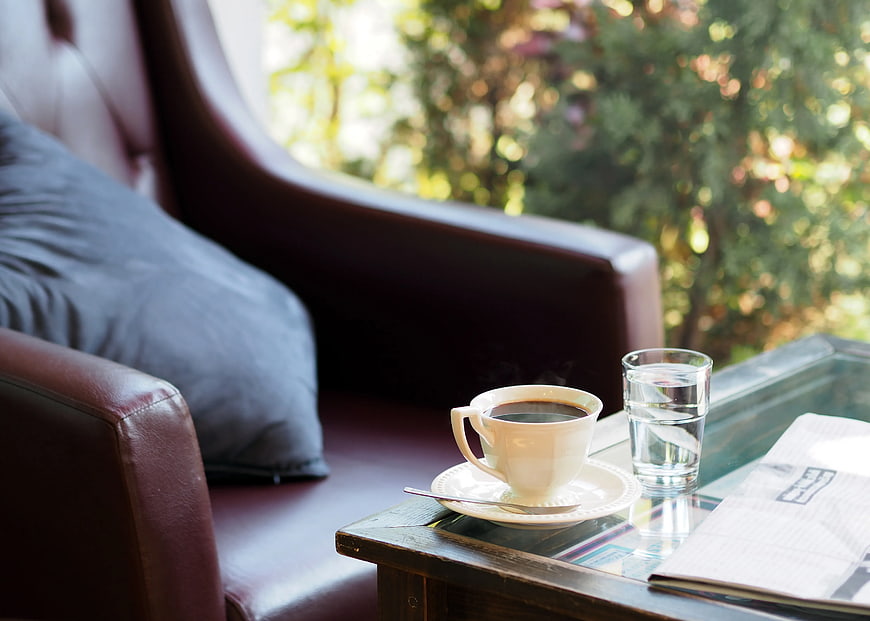 Steaming Coffee Cup and Newspaper on Glass Table