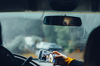 Woman holding smartphone with selfie photo inside rainy car