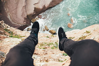 First-person view of legs dangling over coastal cliff