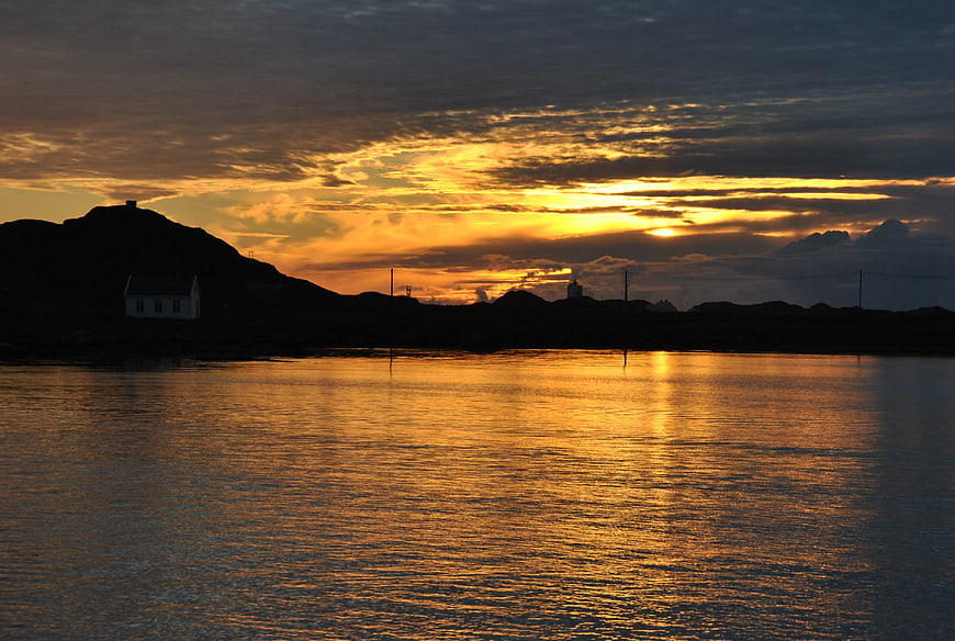 Golden sunset over calm sea with silhouetted coastal village